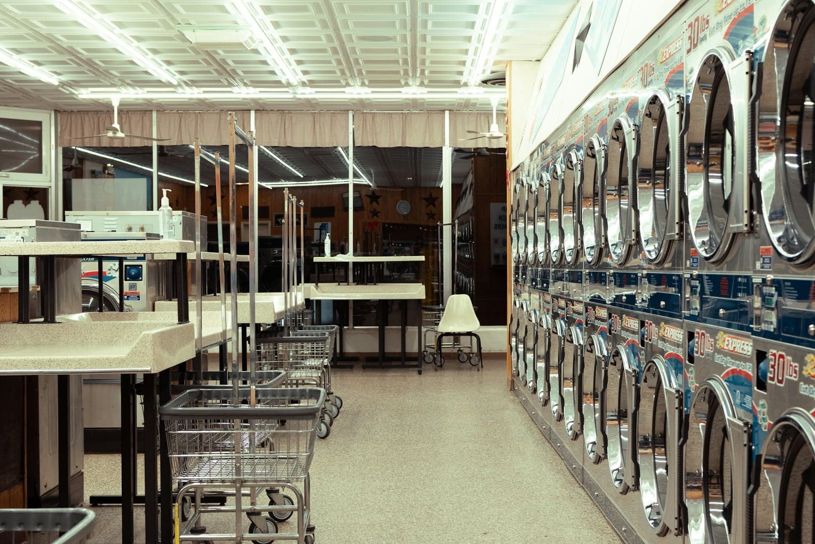 Laundromat interior with stacked machines, folding tables and laundry carts